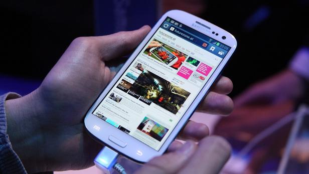 Eine Hand hält ein Samsung-Smartphone, das an ein Ladegerät angeschlossen ist und die Website futurezone.at anzeigt.