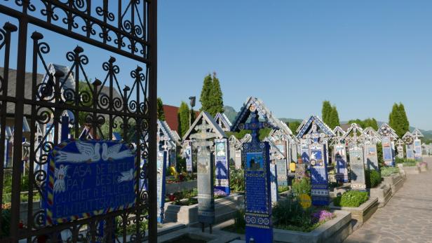 Blick durch ein verziertes Tor auf den Fröhlichen Friedhof in Rumänien mit seinen bunten Grabsteinen.