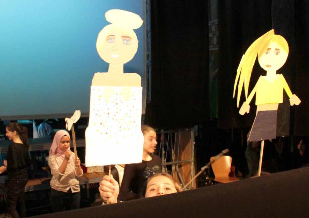 Kinder führen ein Puppentheater mit selbstgebastelten Figuren auf einer Bühne auf.