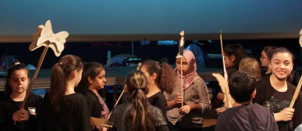 Eine Gruppe von Jugendlichen hält hölzerne Stabpuppen auf einer Bühne.