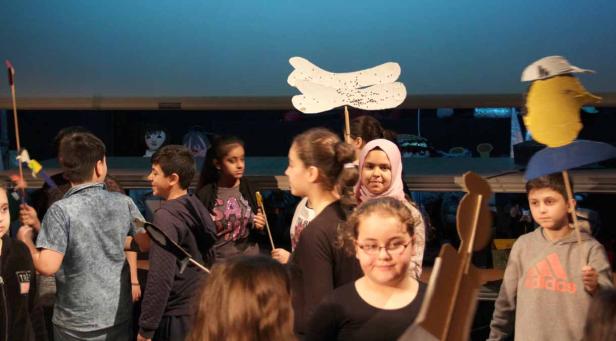 Eine Gruppe von Kindern spielt mit selbstgemachten Requisiten auf einer Bühne.