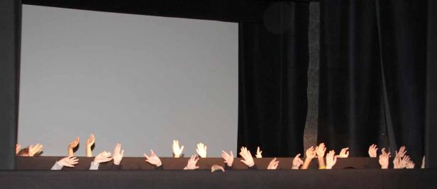 Viele Hände ragen über den Rand einer Bühne vor einem grauen Hintergrund.