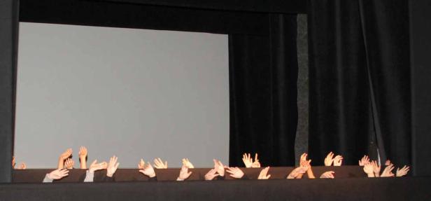 Viele Hände ragen über den Rand einer Bühne vor einem grauen Hintergrund.