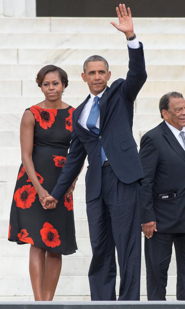 Barack Obama und Michelle Obama stehen Händchen haltend auf einer Treppe, während Obama winkt.