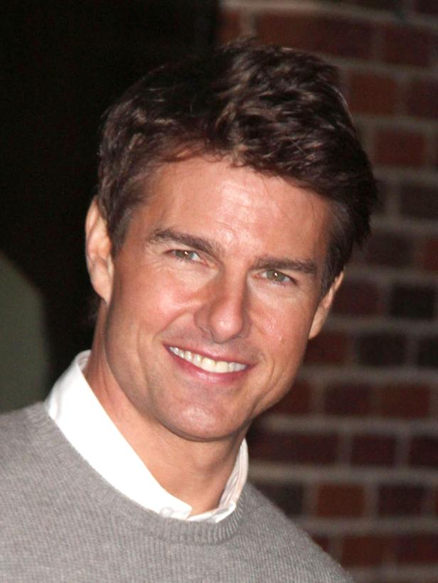 Ein lächelnder Tom Cruise vor einer Backsteinmauer.