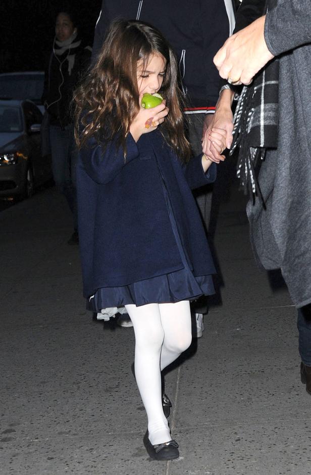 Ein junges Mädchen isst einen grünen Apfel, während es Händchen hält.