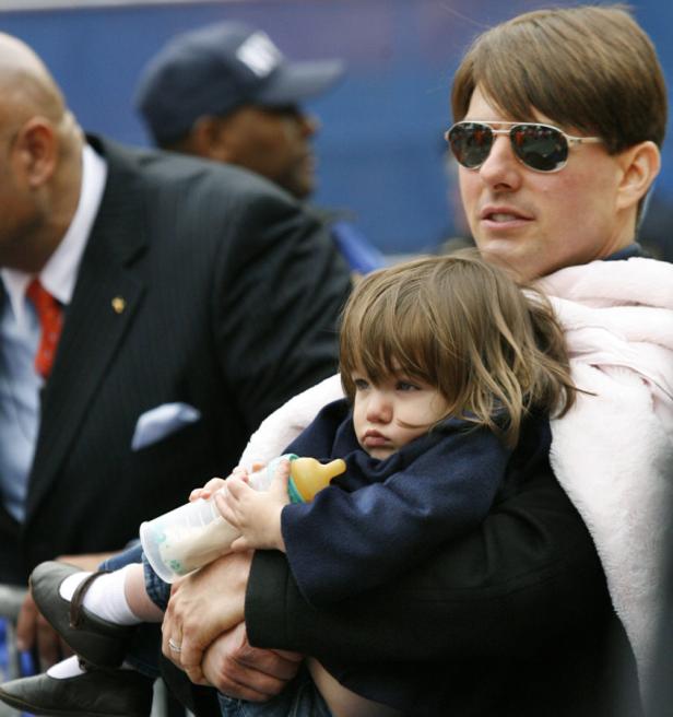 Tom Cruise hält seine Tochter Suri im Arm, die eine Milchflasche hält.