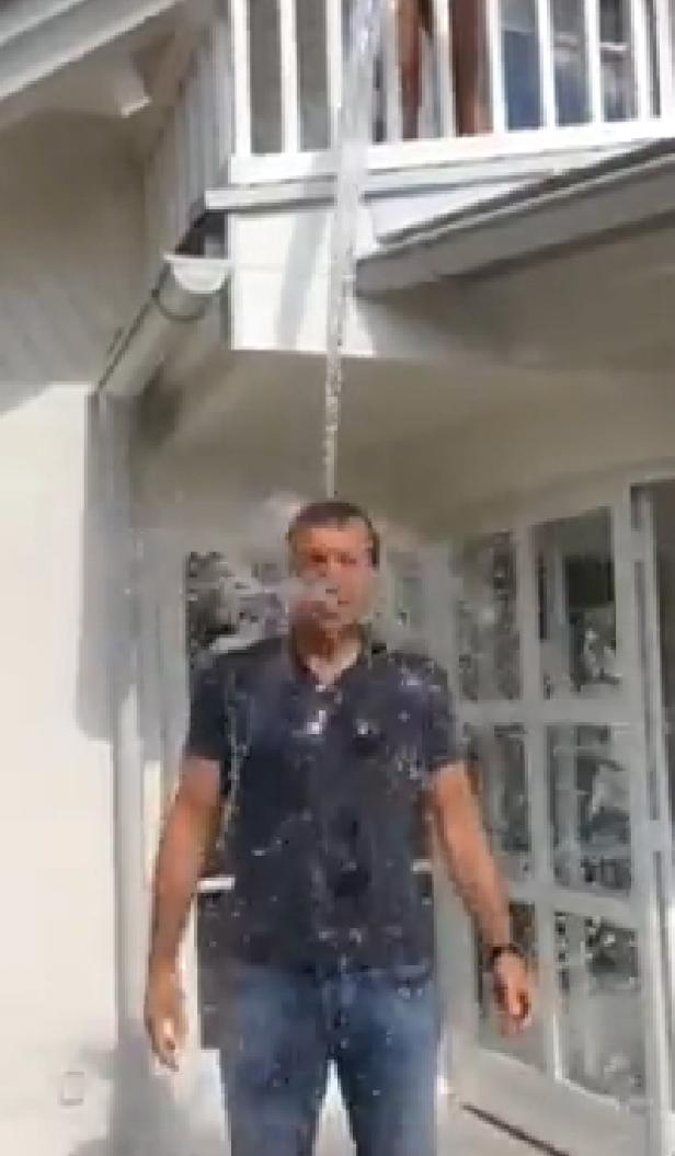 Ein Mann wird von einer Person auf einem Balkon mit Wasser übergossen.