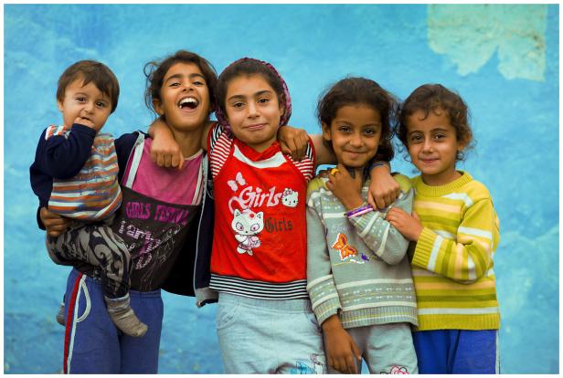 Fünf lächelnde Kinder stehen vor einer blauen Wand.