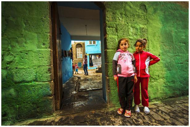 Zwei Mädchen stehen vor einer grün gestrichenen Mauer in einer Gasse.