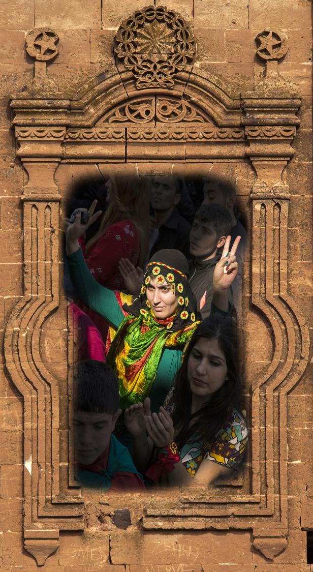 Eine Frau in traditioneller Kleidung gestikuliert vor einer Gruppe von Menschen in einem verzierten Steintorbogen.