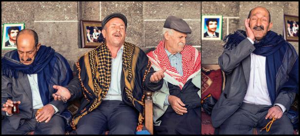 Vier ältere Männer sitzen beieinander, einige tragen traditionelle Kopfbedeckungen und Tücher.