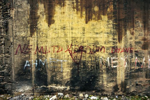 Eine beschmierte und verwitterte Betonwand mit Graffiti in Rot und Weiß.