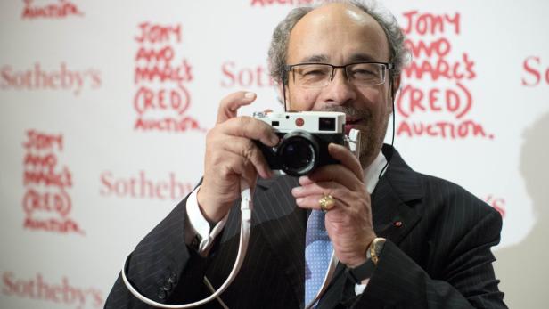 Ein Mann mit Brille fotografiert mit einer Leica Kamera vor einem Hintergrund mit „Sotheby's“-Logos.