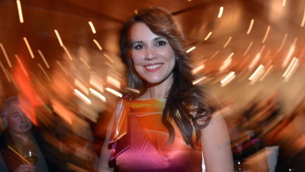 Eine lächelnde Frau in einem farbenfrohen Kleid auf einer Veranstaltung.