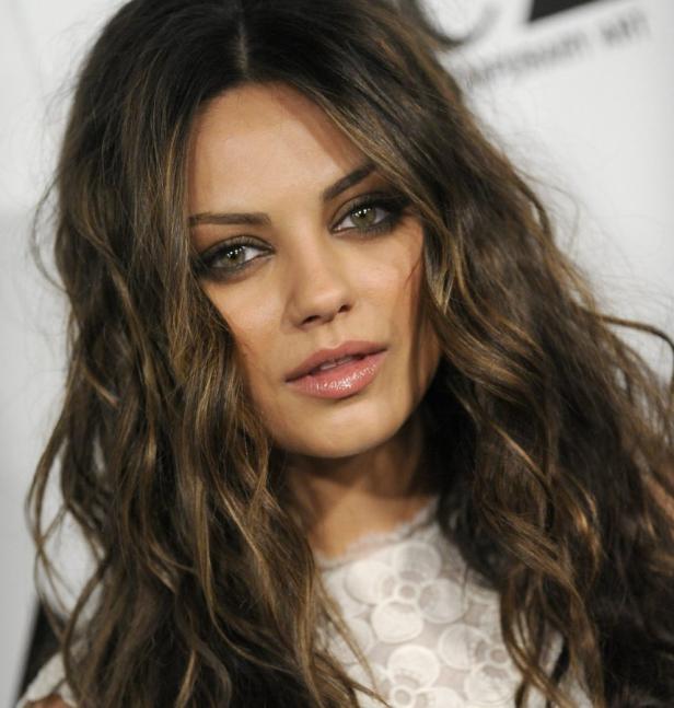 Porträt von Mila Kunis mit gewelltem, braunem Haar und hellem Kleid.