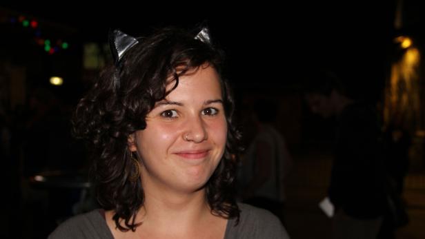 Eine Frau mit lockigem Haar und Katzenohren lächelt in die Kamera.