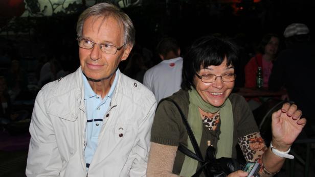 Ein älteres Paar sitzt zusammen und lächelt in die Kamera.