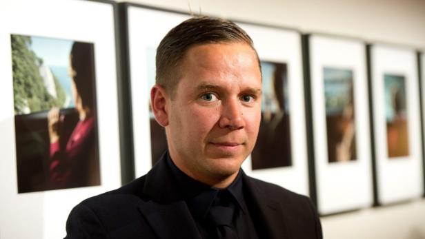 Ein Mann in einem dunklen Anzug steht vor einer Reihe gerahmter Fotografien.