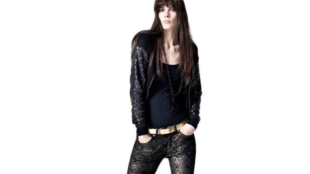 Eine Frau mit dunklen Haaren trägt eine paillettenbesetzte Jacke und goldene Hosen.