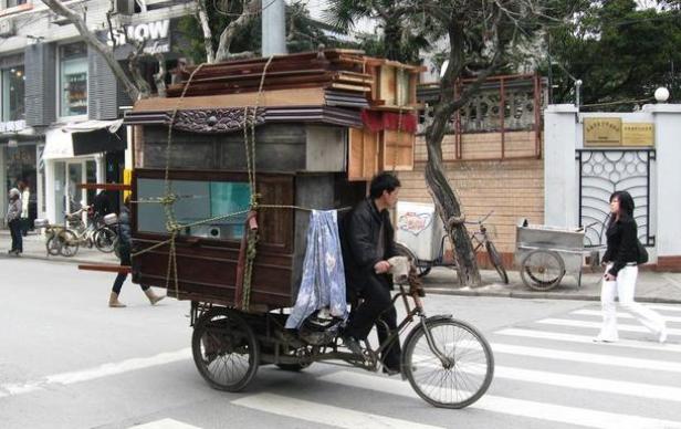 Ein Mann transportiert Möbelstücke auf einem Fahrrad über einen Zebrastreifen.