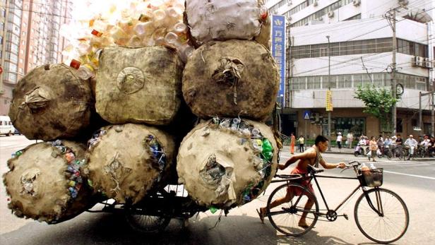Ein Mann zieht einen Karren voller recycelter Plastikflaschen mit seinem Fahrrad durch eine Stadt.