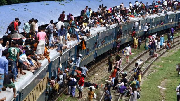 Ein überfüllter Zug mit Menschen auf den Waggons und Gleisen.