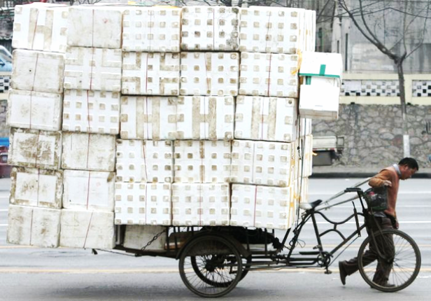 Ein Mann schiebt ein Fahrrad mit Anhänger, der mit weißen Styroporkisten beladen ist.