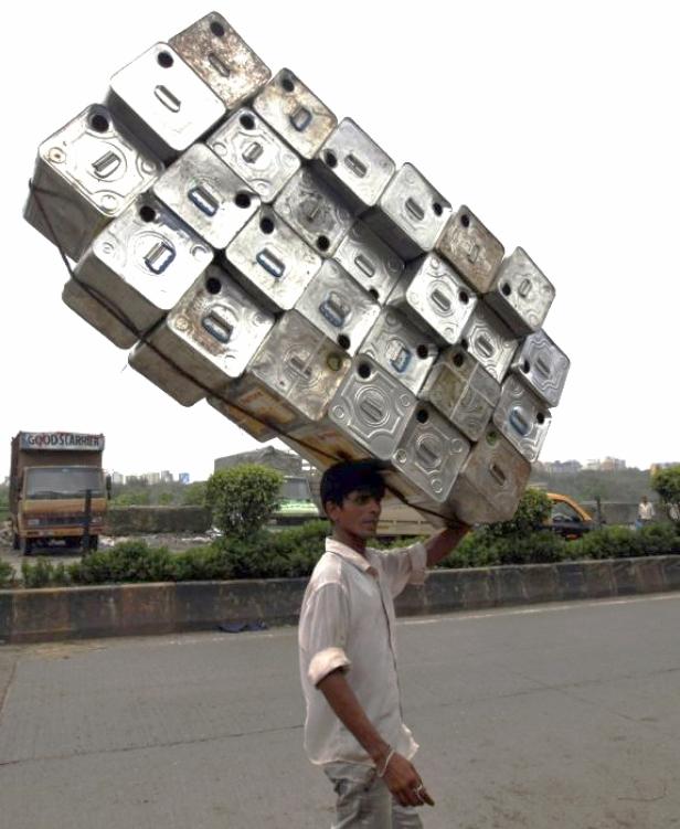Ein Mann trägt einen großen Stapel silberner Behälter auf seinem Kopf.