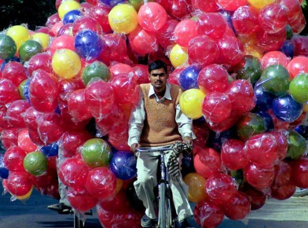 Ein Mann fährt mit einem Fahrrad, das mit vielen bunten Ballons beladen ist.