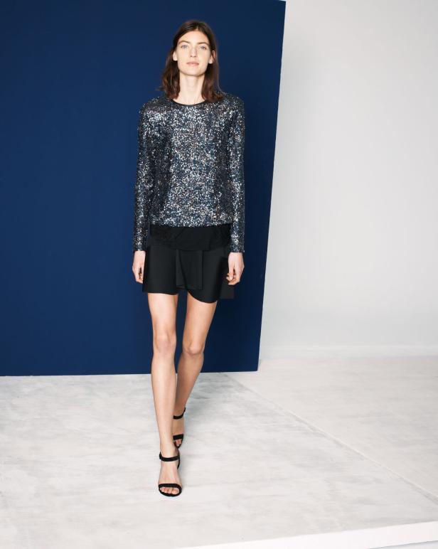 Eine Frau mit einem Paillettenoberteil und einem schwarzen Rock vor einem blauen Hintergrund.