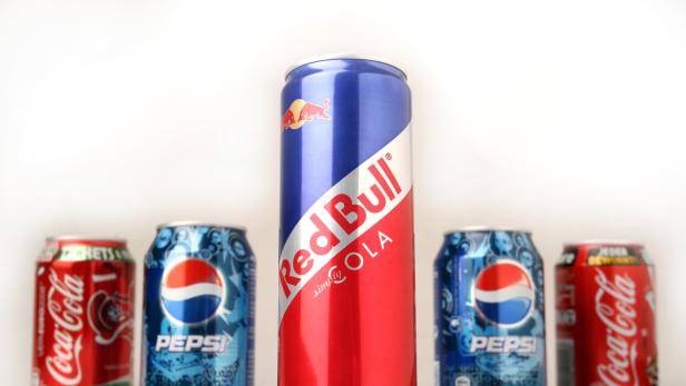 Mehrere Dosen Coca-Cola, Pepsi und Red Bull Cola stehen vor einem weißen Hintergrund.