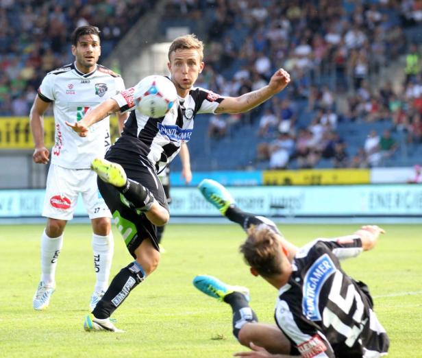 Ein Fußballspieler schießt den Ball, während ein anderer zu Boden geht.