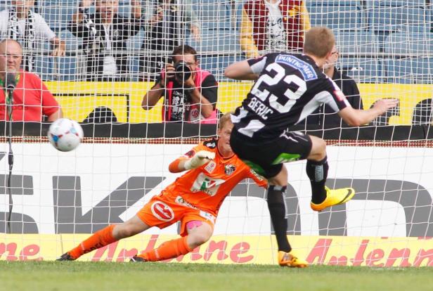 Ein Fußballspieler schießt den Ball, während der Torwart versucht, ihn abzuwehren.