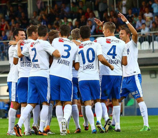 Eine Gruppe Fußballspieler in weißen und blauen Trikots umarmt sich auf dem Spielfeld.