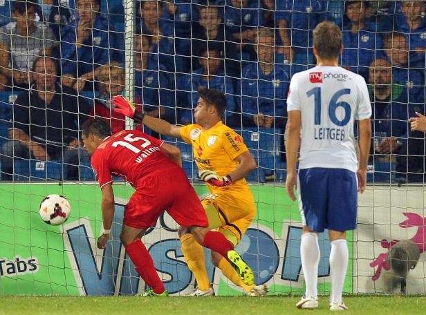 Ein Fußballspieler schießt den Ball ins Tor, während der Torwart versucht, ihn abzuwehren.