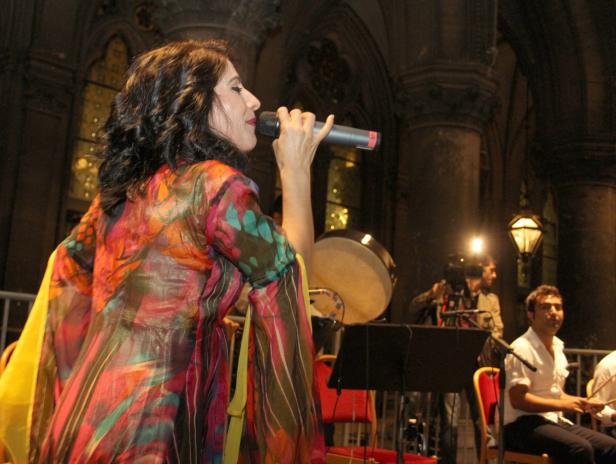 Eine Sängerin tritt mit einem Mikrofon vor einer Band auf einer Bühne auf.