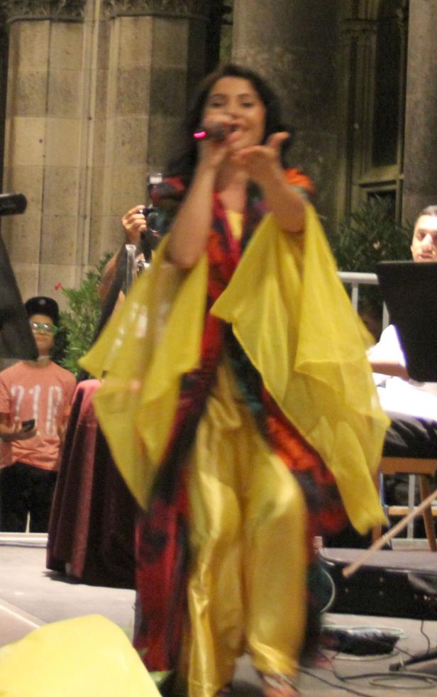 Eine Sängerin tritt in einem gelb-roten Kostüm auf einer Bühne auf.