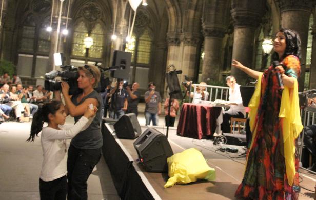 Eine Sängerin tritt auf einer Bühne vor Publikum auf, während sie gefilmt wird.