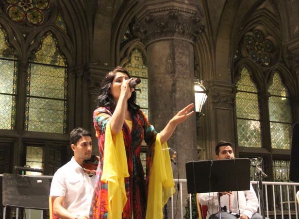 Eine Sängerin tritt mit Band in einem Gebäude mit großen Bogenfenstern auf.