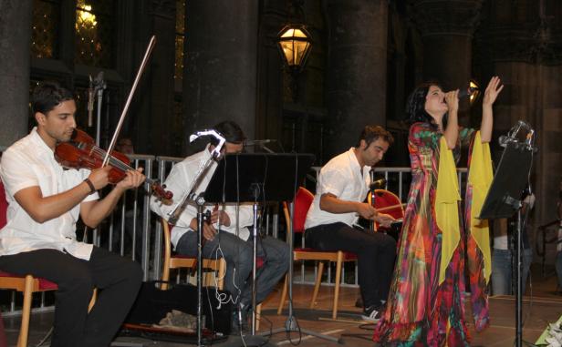 Eine Band spielt live mit Geige, Bratsche, Schlagzeug und einer Sängerin in einem bunten Kleid.