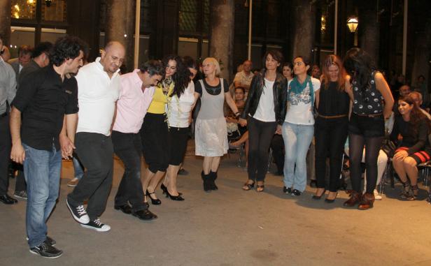 Eine Gruppe von Menschen tanzt im Freien im Kreis Hand in Hand.