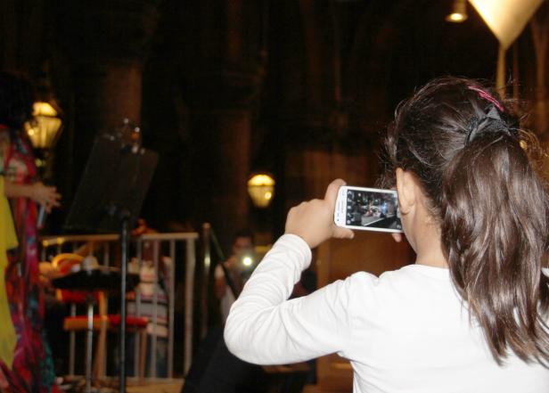 Ein Mädchen filmt mit ihrem Smartphone eine Band auf einer Bühne.