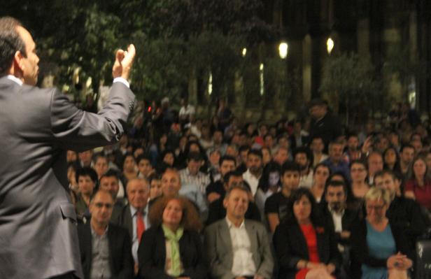 Ein Mann in Anzug spricht vor einer großen Menschenmenge im Freien.