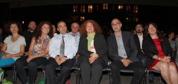 Eine Gruppe von Menschen sitzt bei einer Veranstaltung im Freien nebeneinander.