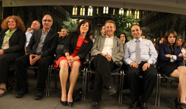 Eine Gruppe von Menschen sitzt auf Stühlen vor einer beleuchteten Fassade.