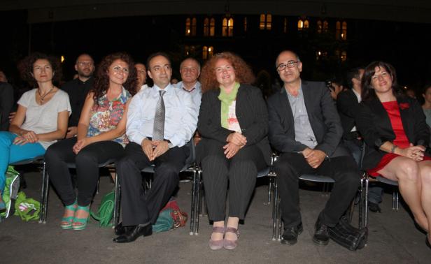 Eine Gruppe von Menschen sitzt bei einer Veranstaltung im Freien nebeneinander.