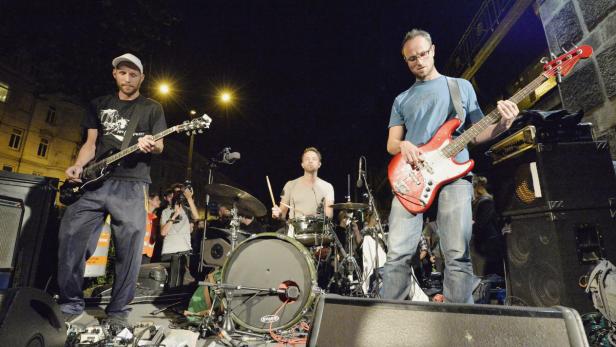 Eine Band spielt nachts live auf einer Bühne vor Publikum.