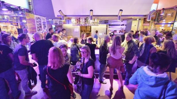 Viele Menschen stehen und sitzen an einer Bar in einem belebten Lokal.