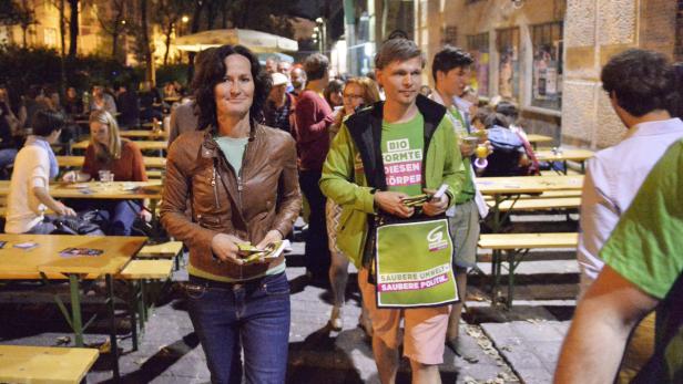 Zwei Personen verteilen Flyer für „Die Grünen“ auf einer belebten Straße.